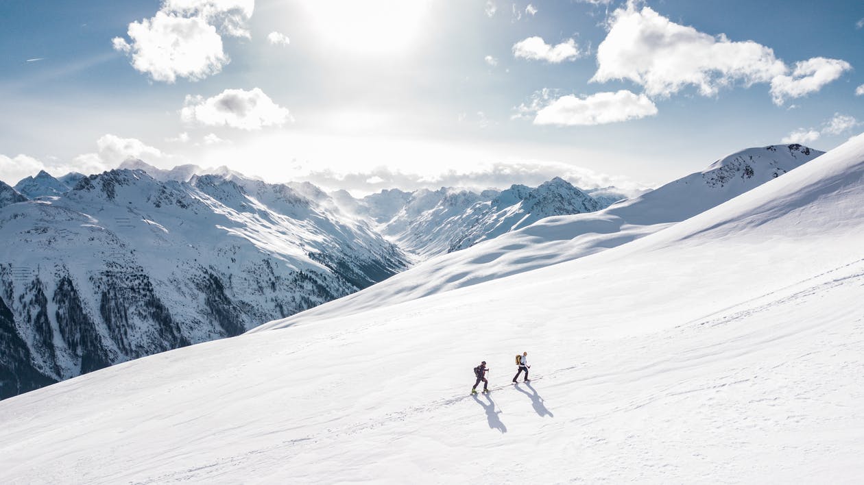 Two people skiing on a mountain slope with the sun shining.